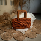 Brown woven handbag with wooden handle on a textured surface